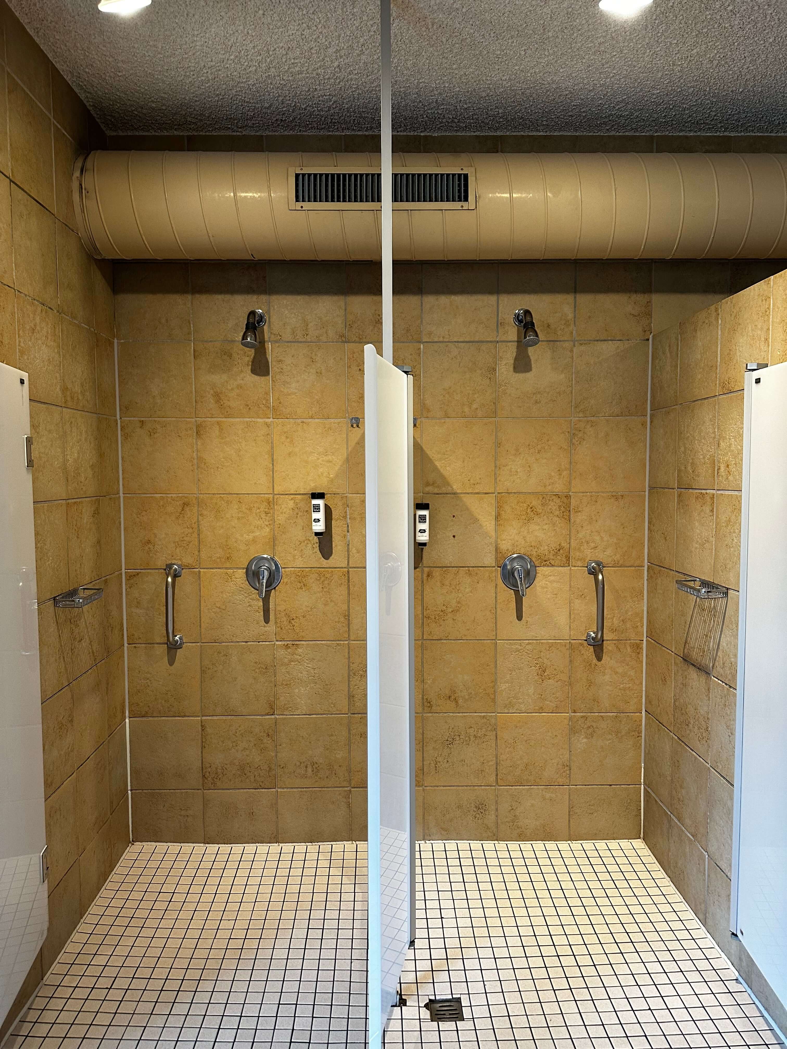 Duschen im Schwimmbadbereich des Waldhotel Bärenstein mit beigen Fliesen, Duschköpfen und Haltegriffen – bereit für eine erfrischende Dusche vor oder nach dem Schwimmen.