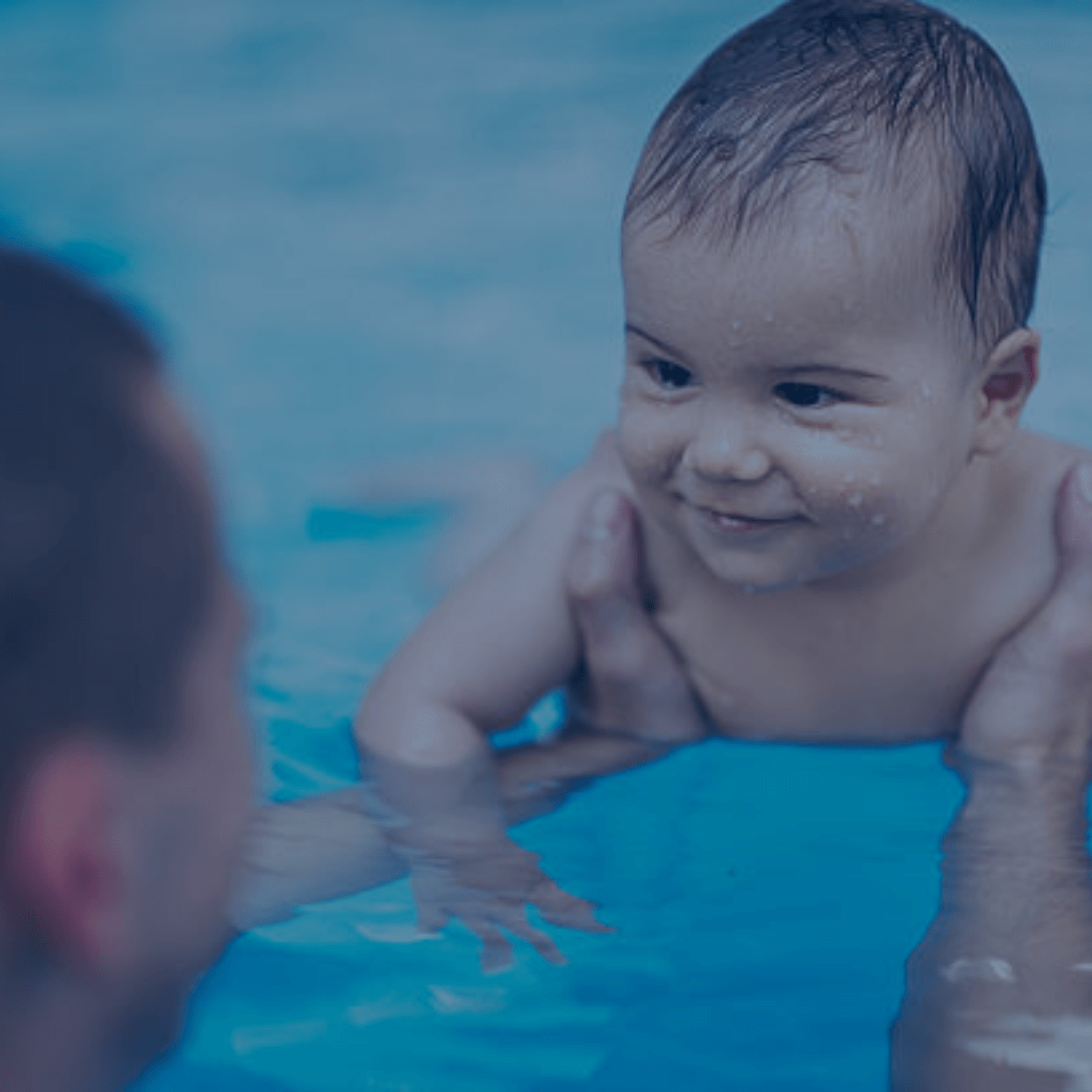Lächelndes Baby im Wasser, das von einer erwachsenen Hand gehalten wird – ideal für frühkindliche Wassergewöhnungskurse.