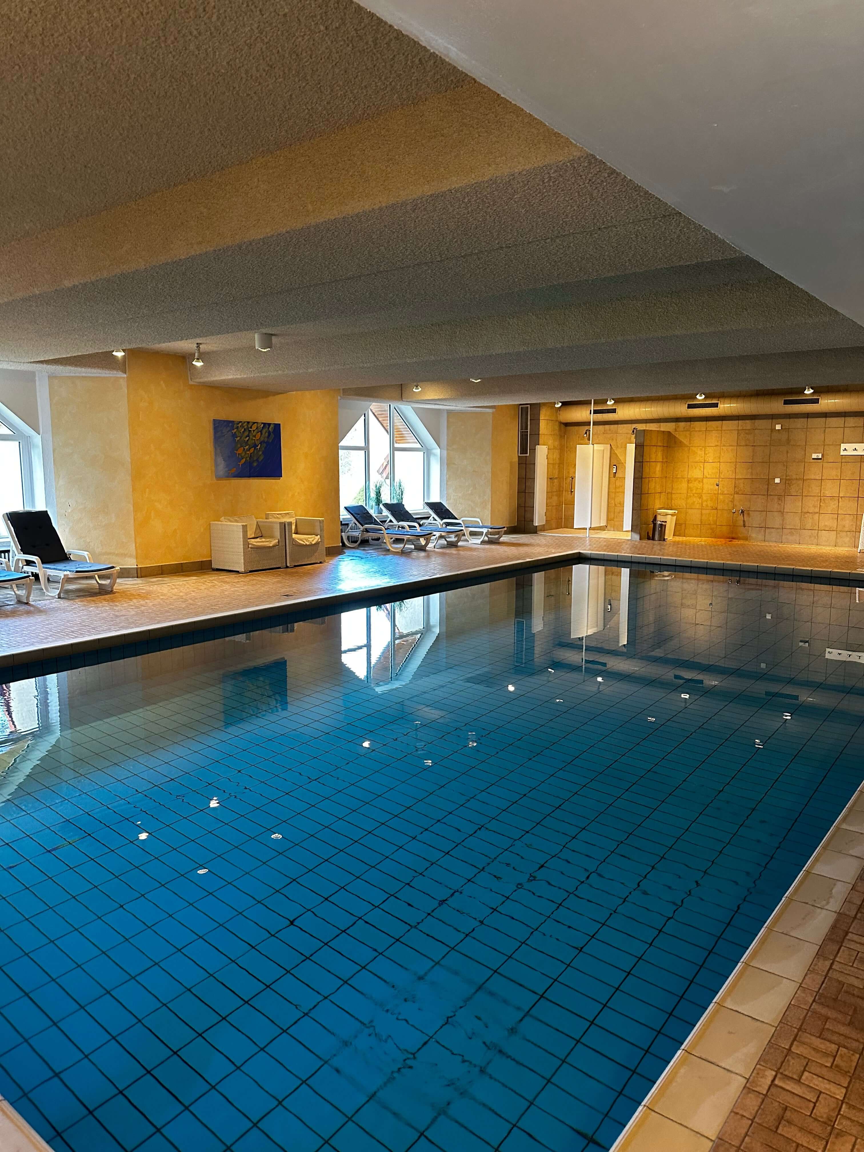 Hallenbad des Waldhotel Bärenstein mit großem rechteckigem Becken, bequemen Liegen und einer warmen, einladenden Atmosphäre.