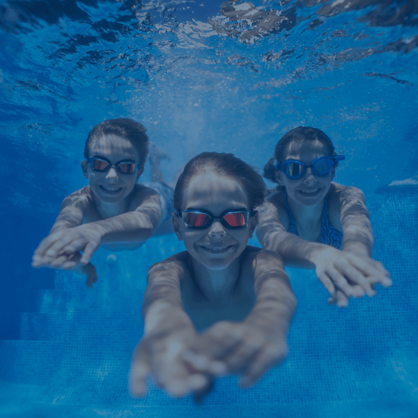 Drei fröhliche Kinder mit Schwimmbrillen tauchen unter Wasser und lächeln – perfekte Ausrüstung für jedes Schwimmlevel.