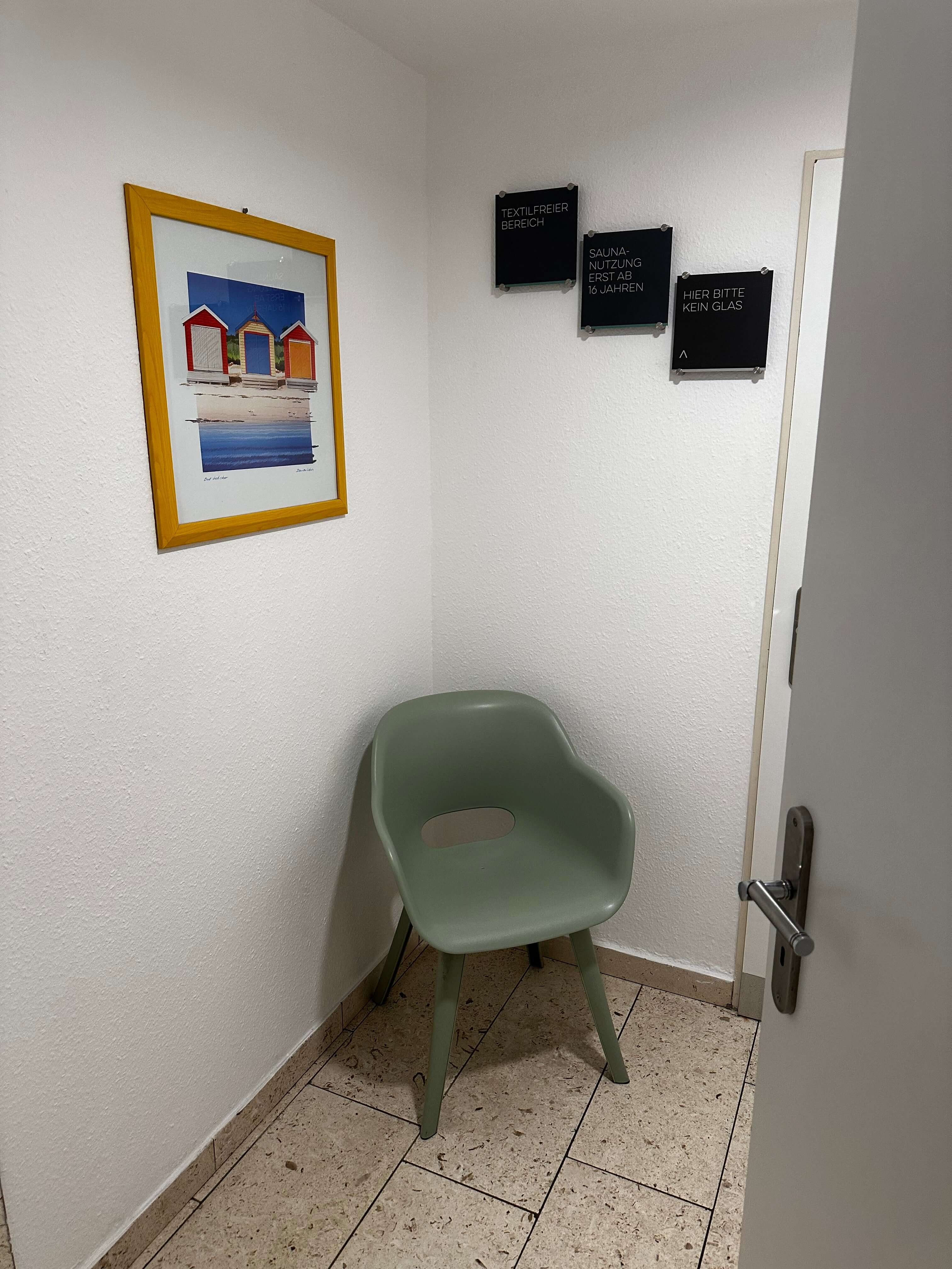 Private Umkleidemöglichkeit mit grünem Stuhl, dekorativem Bild an der Wand und diskretem Bereich für mehr Komfort.