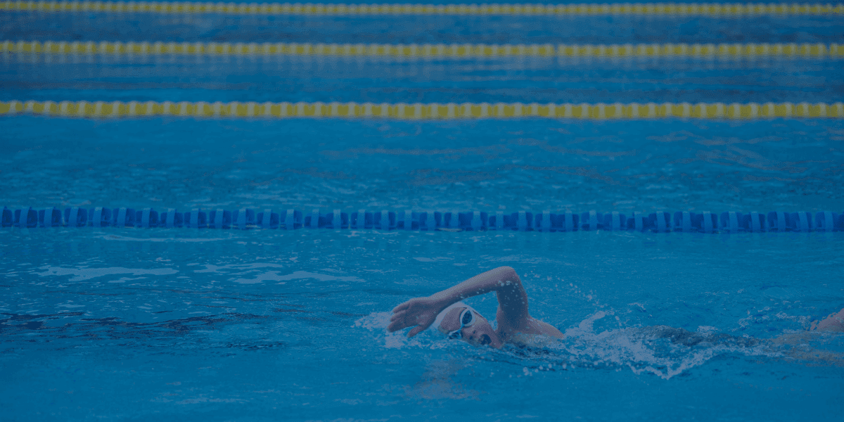 Schwimmer in einem blauen Pool, der fokussiert seine Technik verbessert – passend zu den 5 Tipps, um schneller schwimmen zu lernen.