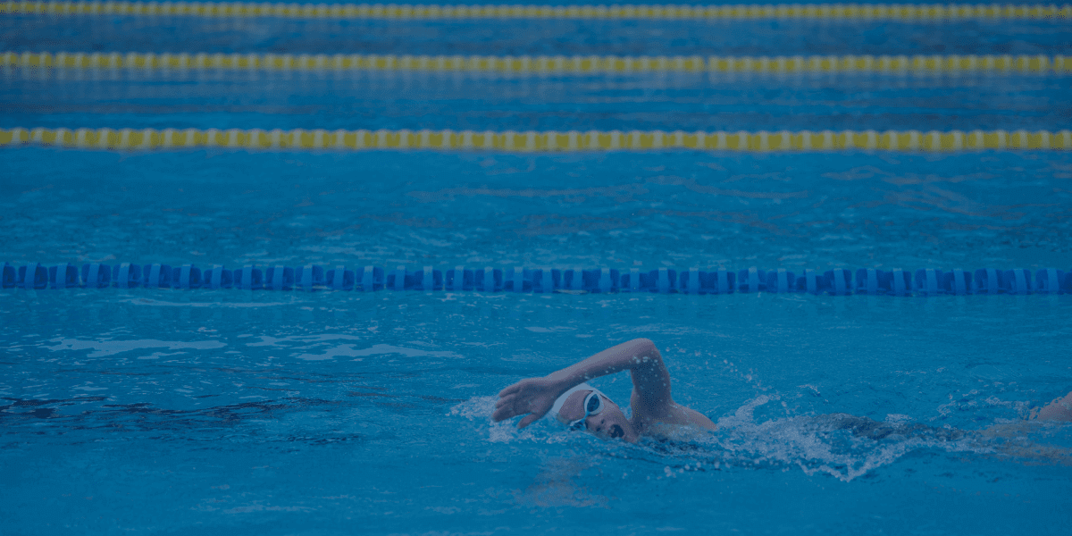 Schwimmer in einem blauen Pool, der fokussiert seine Technik verbessert – passend zu den 5 Tipps, um schneller schwimmen zu lernen.