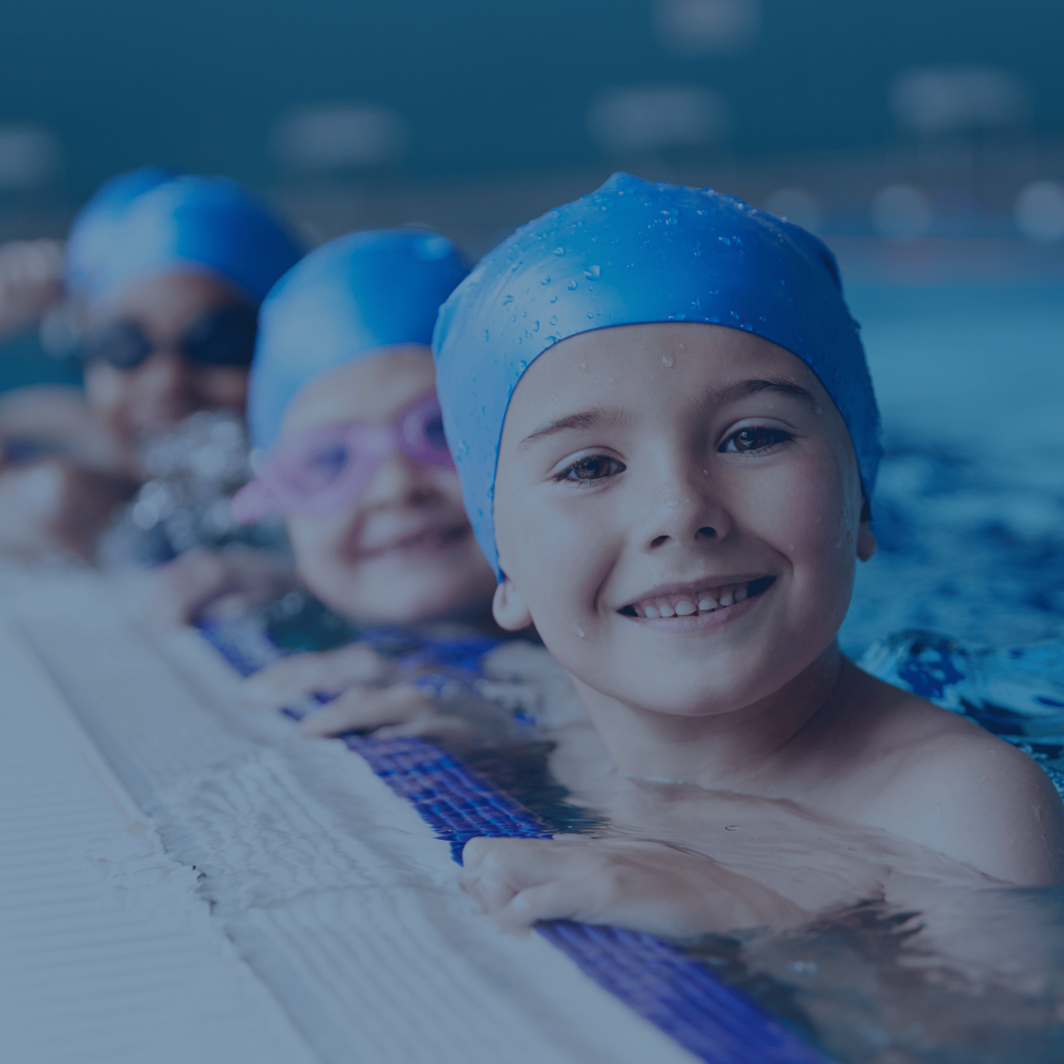 Lächelnde Kinder mit Schwimmkappen im Wasser – Anfängerkurs bei AquaFit mit der Möglichkeit, das Seepferdchen- und Seeräuber-Abzeichen zu erreichen.