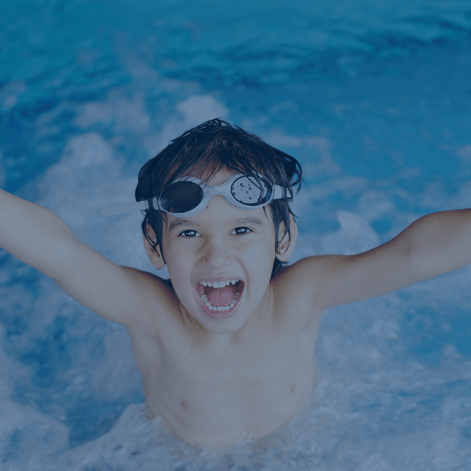 Lächelnder Junge mit Schwimmbrille hebt die Arme vor Freude im Schwimmbecken – Spaß und Sicherheit im Wasser.