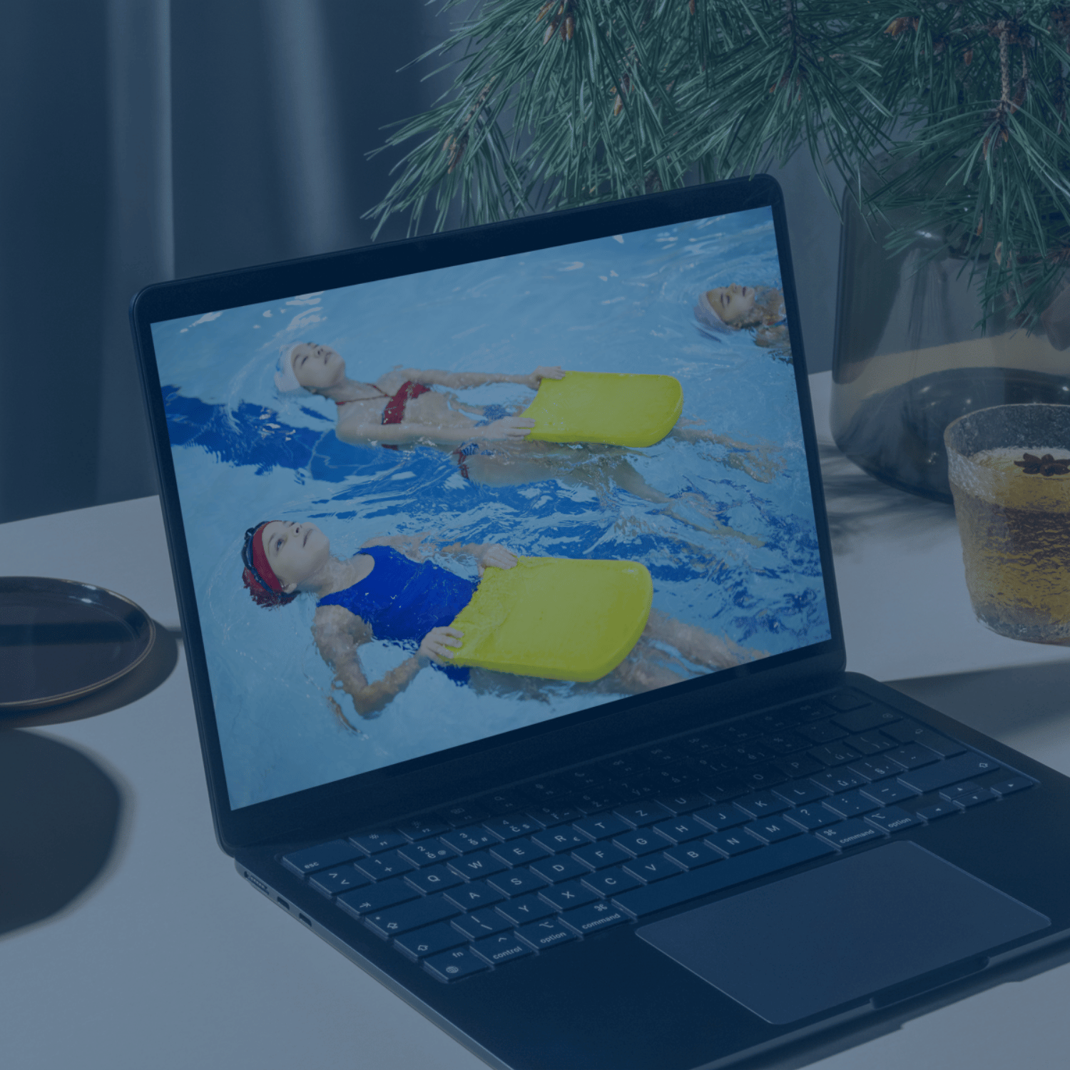 Ein Laptop zeigt eine Szene aus einem Schwimmkurs, bei dem Kinder mit gelben Schwimmbrettern im Wasser üben – ideal für die Online-Schwimmkurse von AquaFit.