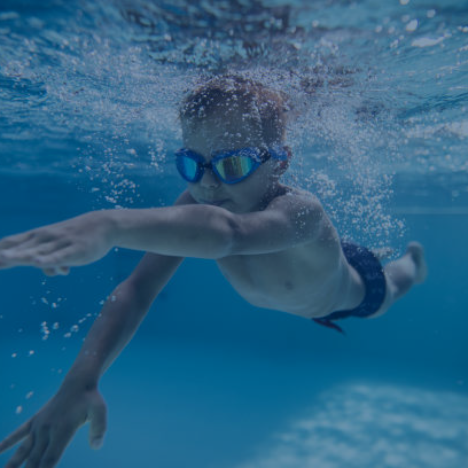 Kind mit Schwimmbrille taucht unter Wasser – Anfängerkurse zur Förderung der Wasserfreude.